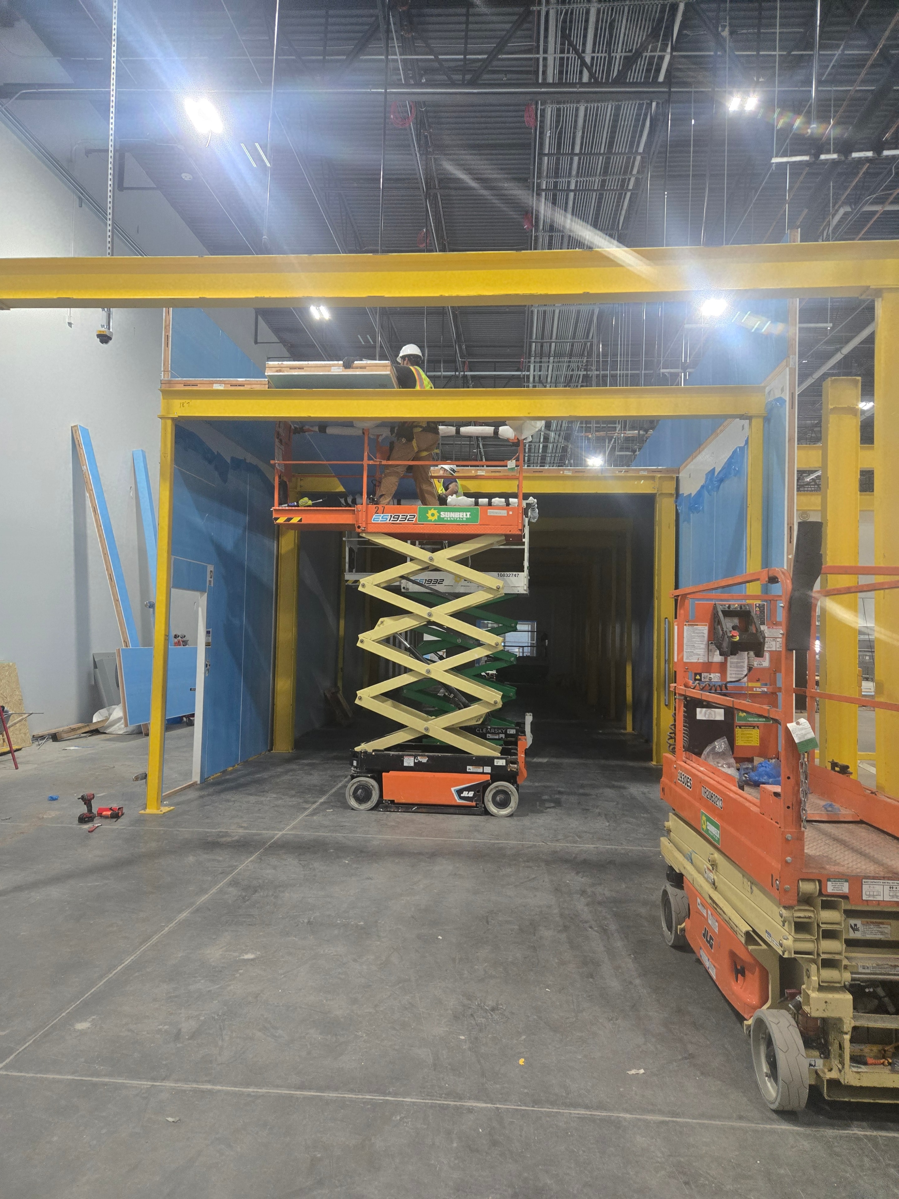 Workers installing walk-in cooler door frame with scissor lift inside Amazon facility